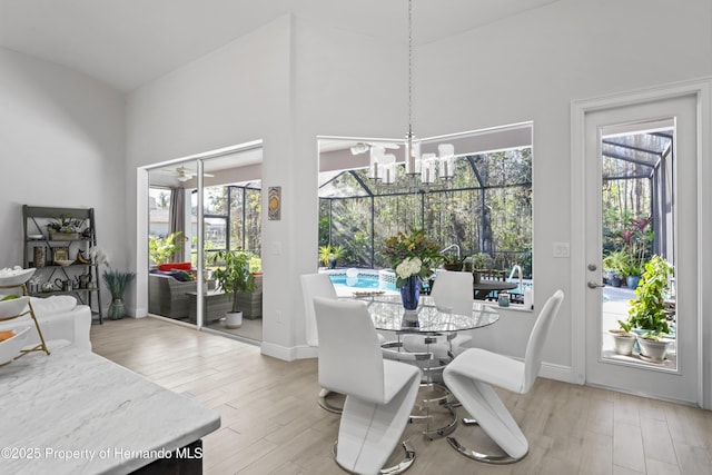 dining area featuring ceiling fan with notable chandelier, light hardwood / wood-style floors, and a high ceiling