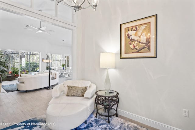 sitting room featuring hardwood / wood-style floors, ceiling fan with notable chandelier, and a high ceiling