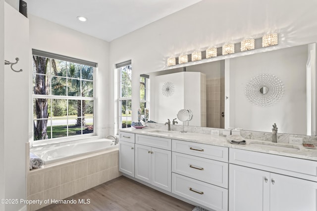 bathroom with vanity, wood-type flooring, and a relaxing tiled tub