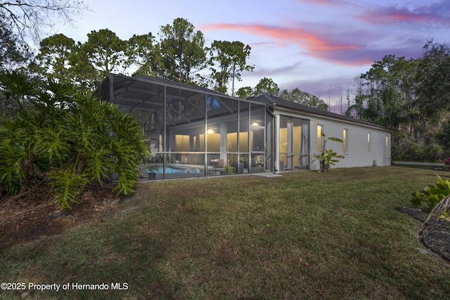 back house at dusk featuring glass enclosure and a yard