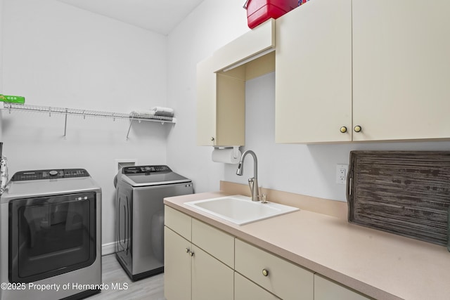 clothes washing area featuring washer and dryer, cabinets, light wood-type flooring, and sink