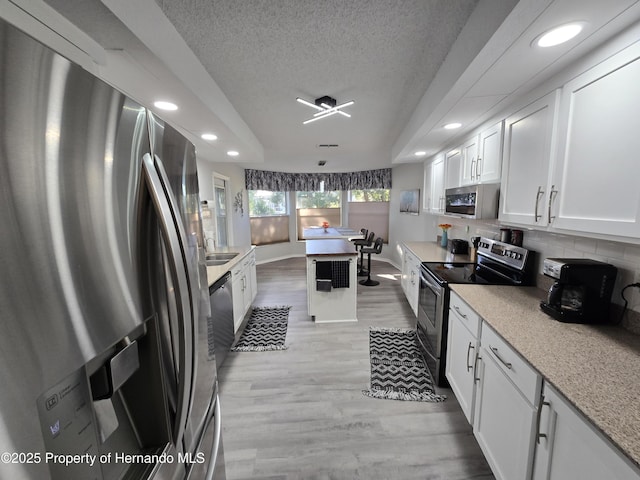 kitchen featuring decorative backsplash, appliances with stainless steel finishes, a textured ceiling, light hardwood / wood-style flooring, and white cabinetry