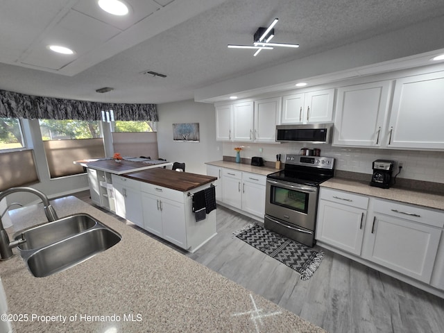 kitchen featuring appliances with stainless steel finishes, a textured ceiling, sink, white cabinets, and butcher block countertops