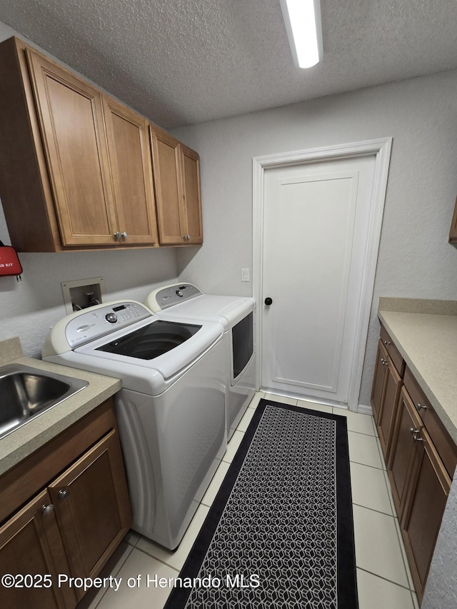 clothes washing area with washer and clothes dryer, cabinets, sink, light tile patterned floors, and a textured ceiling