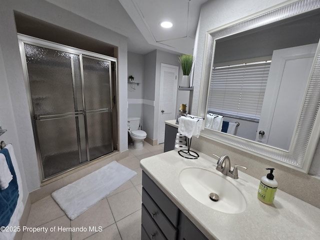 bathroom with tile patterned floors, vanity, toilet, and a shower with door