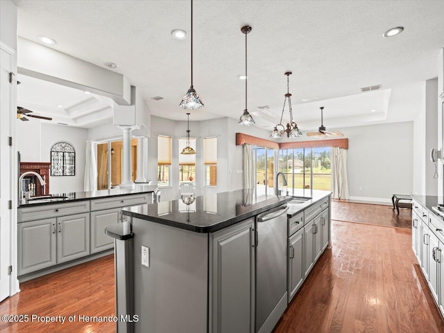 kitchen with gray cabinets, an island with sink, a raised ceiling, and decorative light fixtures