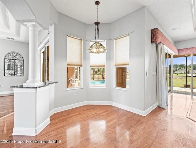 unfurnished dining area with light wood-type flooring, decorative columns, and baseboards