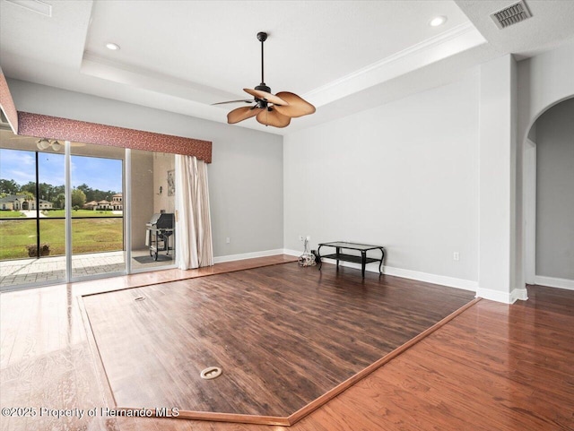 empty room with arched walkways, a tray ceiling, dark wood-type flooring, and visible vents