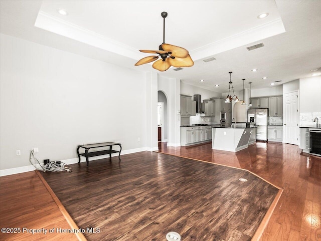 living room featuring visible vents, arched walkways, a ceiling fan, dark wood finished floors, and a tray ceiling