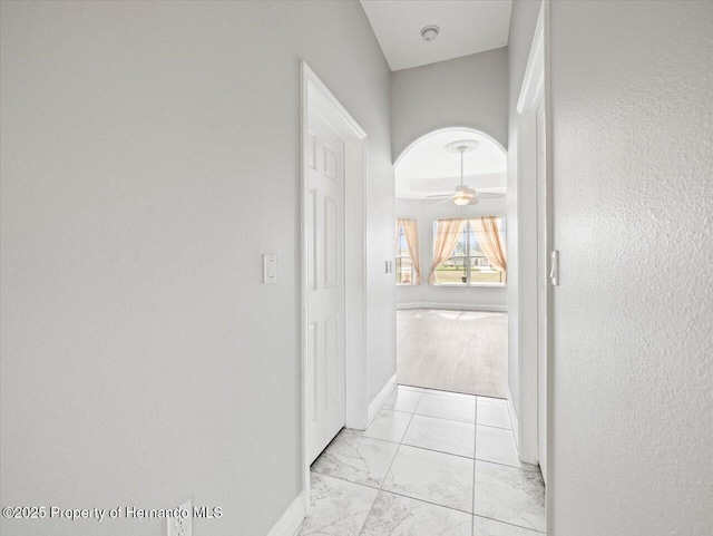 hall featuring arched walkways, marble finish floor, and baseboards