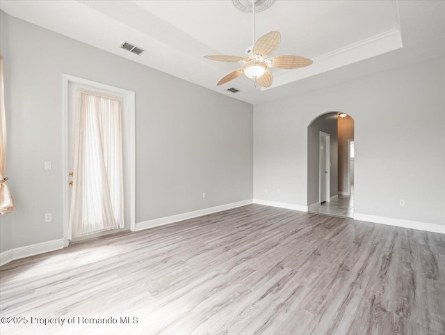 unfurnished room featuring arched walkways, visible vents, baseboards, light wood-style floors, and a raised ceiling