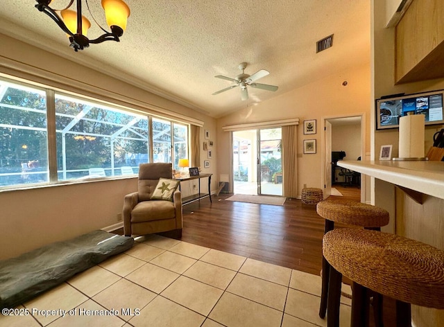 sitting room with a healthy amount of sunlight, lofted ceiling, a textured ceiling, and light tile patterned floors