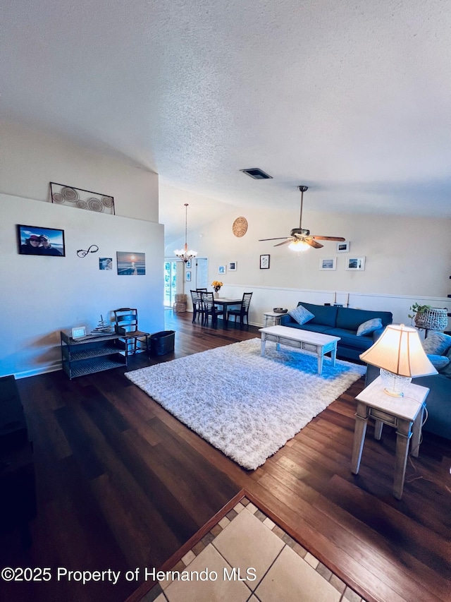 living room featuring a textured ceiling, hardwood / wood-style floors, ceiling fan with notable chandelier, and vaulted ceiling