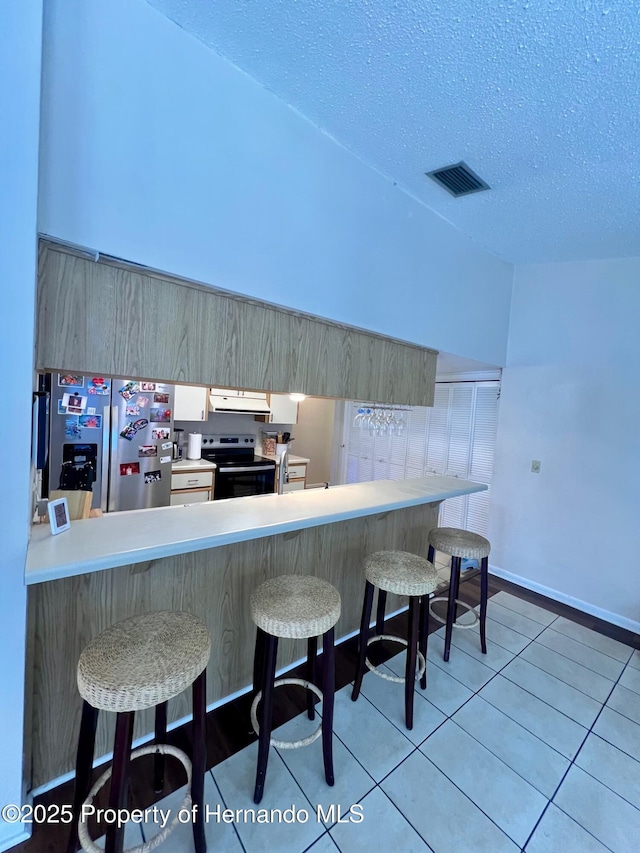 kitchen featuring range hood, stainless steel refrigerator with ice dispenser, kitchen peninsula, a kitchen bar, and electric stove