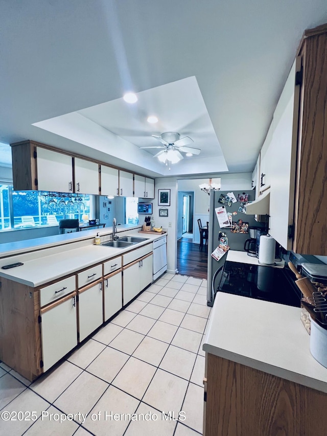 kitchen with white appliances, a raised ceiling, sink, ceiling fan, and white cabinetry