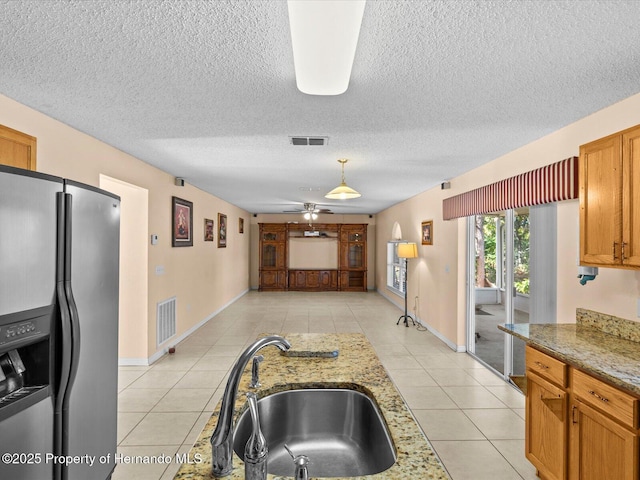 kitchen with sink, ceiling fan, stainless steel fridge, light tile patterned floors, and light stone counters