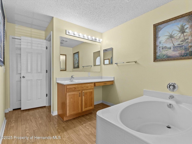 bathroom with hardwood / wood-style flooring, a relaxing tiled tub, a textured ceiling, and vanity