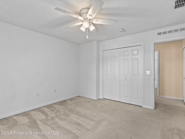 unfurnished bedroom featuring ceiling fan, a closet, light colored carpet, and a textured ceiling