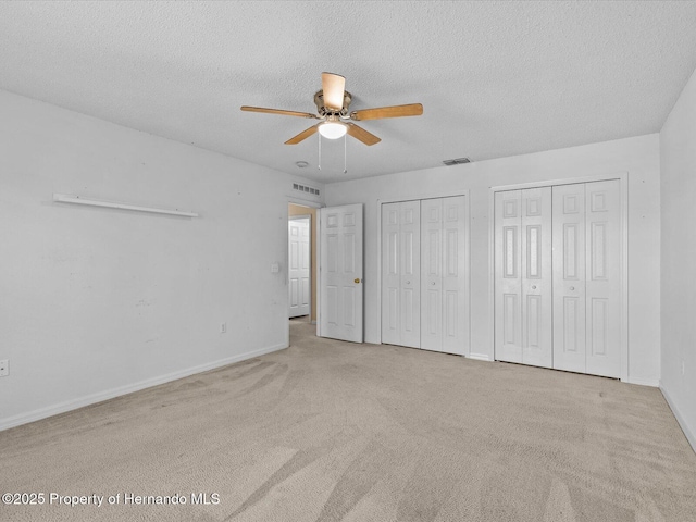 unfurnished bedroom featuring two closets, ceiling fan, light colored carpet, and a textured ceiling