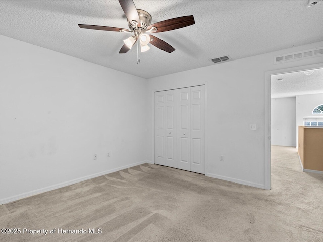 unfurnished bedroom featuring a textured ceiling, ceiling fan, light carpet, and a closet