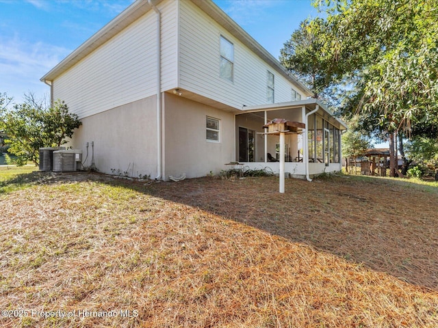 back of property featuring central air condition unit, a sunroom, and a lawn