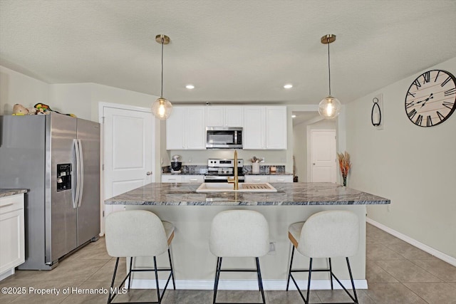 kitchen featuring dark stone countertops, white cabinetry, hanging light fixtures, and appliances with stainless steel finishes