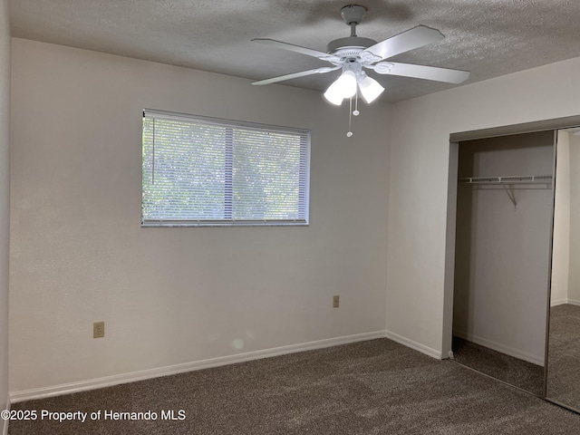 unfurnished bedroom with a textured ceiling, a closet, ceiling fan, and dark colored carpet