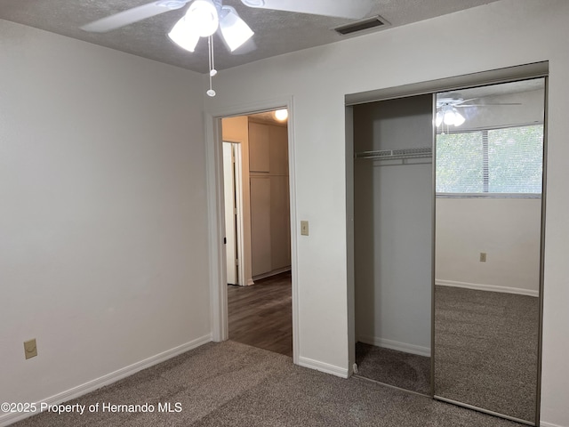 unfurnished bedroom with dark carpet, a textured ceiling, a closet, and ceiling fan