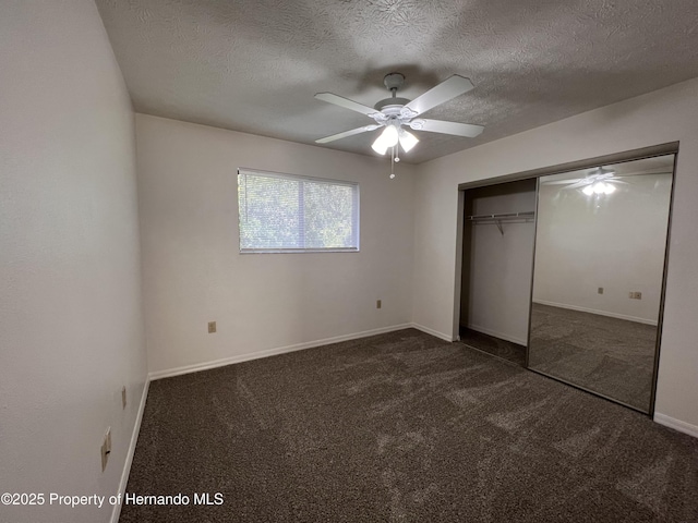 unfurnished bedroom featuring dark carpet, a textured ceiling, a closet, and ceiling fan