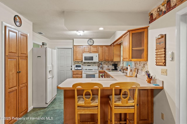 kitchen featuring white appliances, a breakfast bar area, kitchen peninsula, sink, and tasteful backsplash