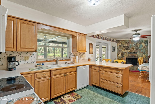 kitchen featuring kitchen peninsula, a textured ceiling, dishwasher, a fireplace, and sink