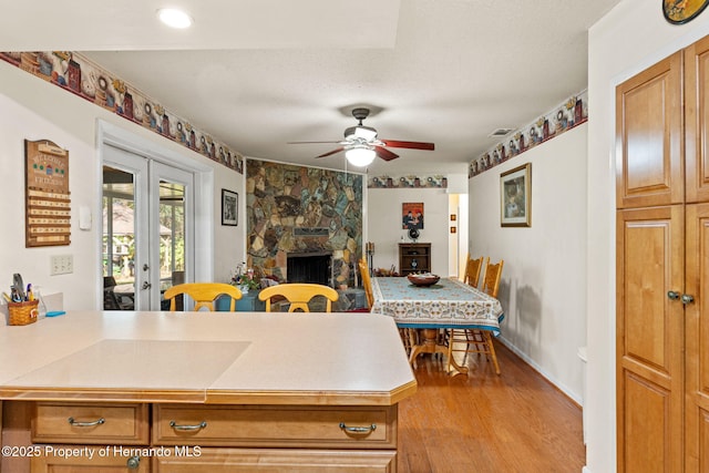 kitchen featuring ceiling fan, french doors, a fireplace, a textured ceiling, and light hardwood / wood-style flooring