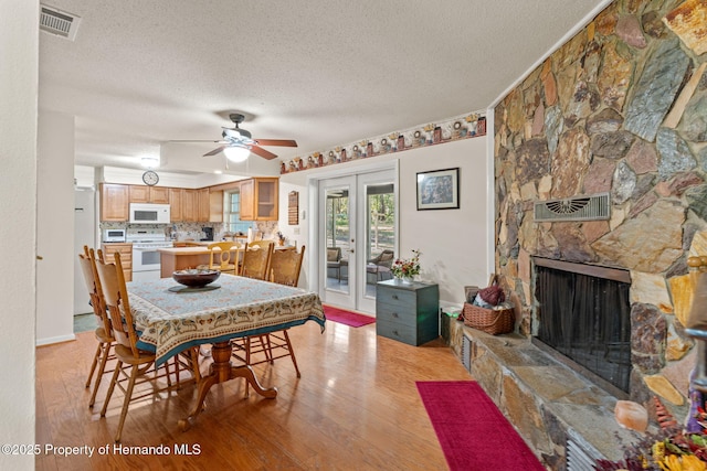 dining room with a fireplace, a textured ceiling, ceiling fan, and light hardwood / wood-style floors