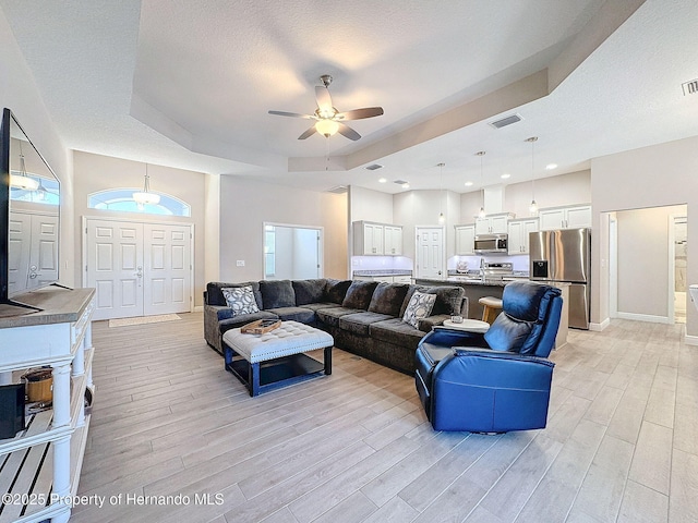 living room featuring ceiling fan, a raised ceiling, a textured ceiling, and light hardwood / wood-style flooring