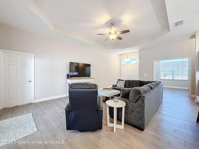 living room featuring a tray ceiling, light hardwood / wood-style flooring, and ceiling fan