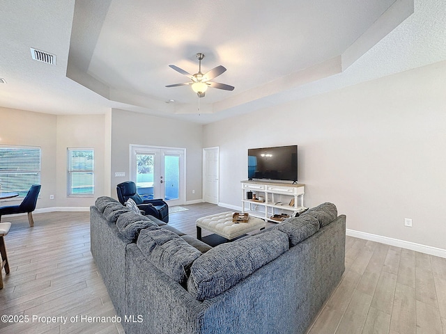 living room with french doors, a tray ceiling, ceiling fan, and light hardwood / wood-style floors