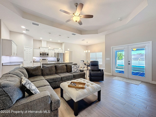 living room with ceiling fan with notable chandelier, a raised ceiling, and french doors