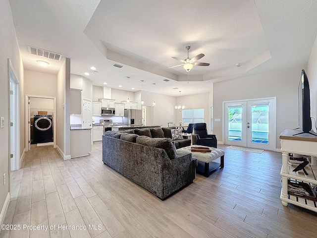 living room featuring washer / dryer, light wood-type flooring, and a tray ceiling