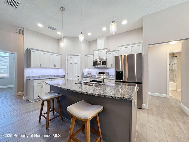 kitchen with a kitchen island with sink, a kitchen breakfast bar, dark stone countertops, decorative light fixtures, and stainless steel appliances