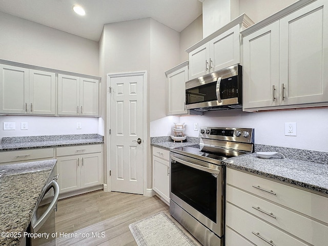 kitchen with light hardwood / wood-style floors, dark stone countertops, and stainless steel appliances