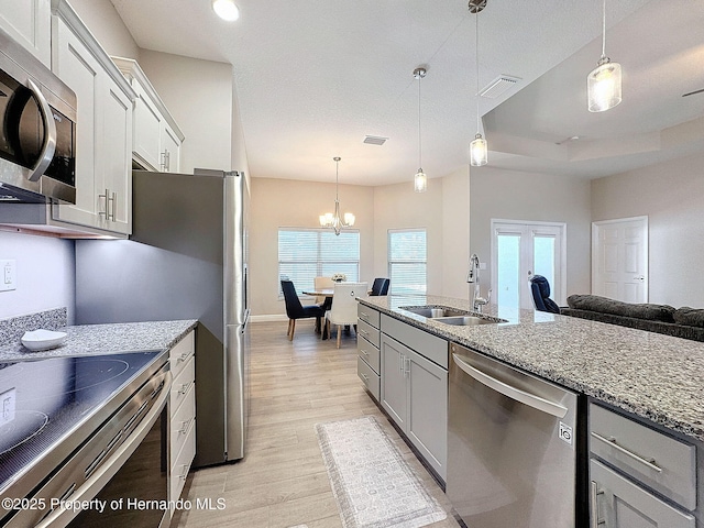 kitchen featuring light stone countertops, sink, stainless steel appliances, pendant lighting, and light wood-type flooring