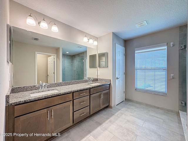 bathroom with tile patterned floors, a shower with door, vanity, and a textured ceiling