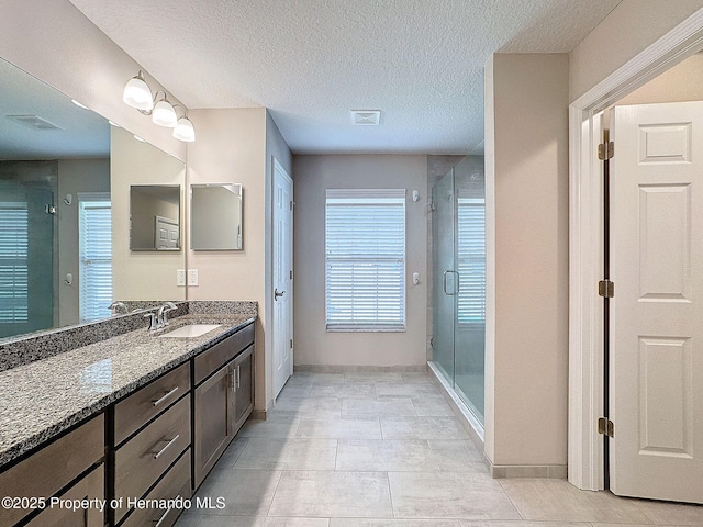 bathroom with tile patterned floors, vanity, a shower with shower door, and a textured ceiling