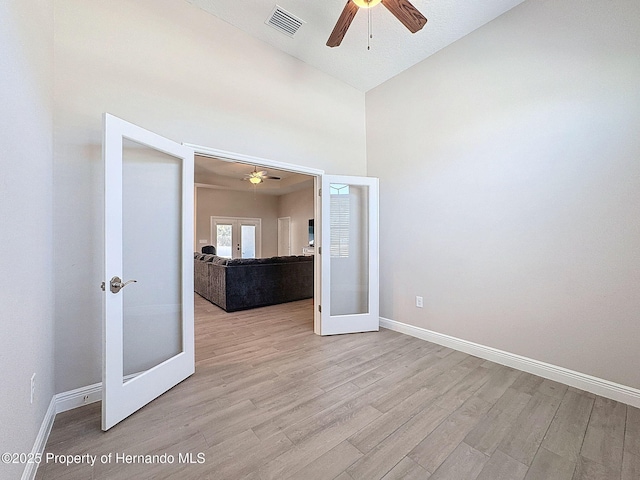 empty room featuring light hardwood / wood-style floors, high vaulted ceiling, and french doors