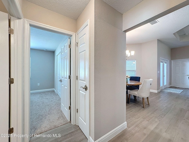 hall with light hardwood / wood-style flooring, a textured ceiling, and a notable chandelier