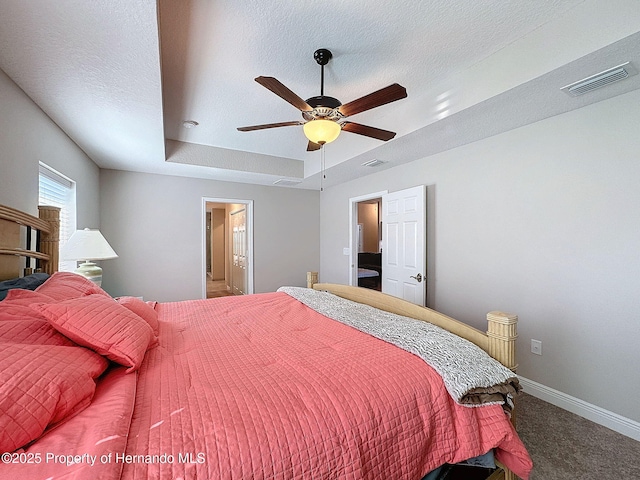 carpeted bedroom with ceiling fan, ensuite bath, a textured ceiling, and a tray ceiling