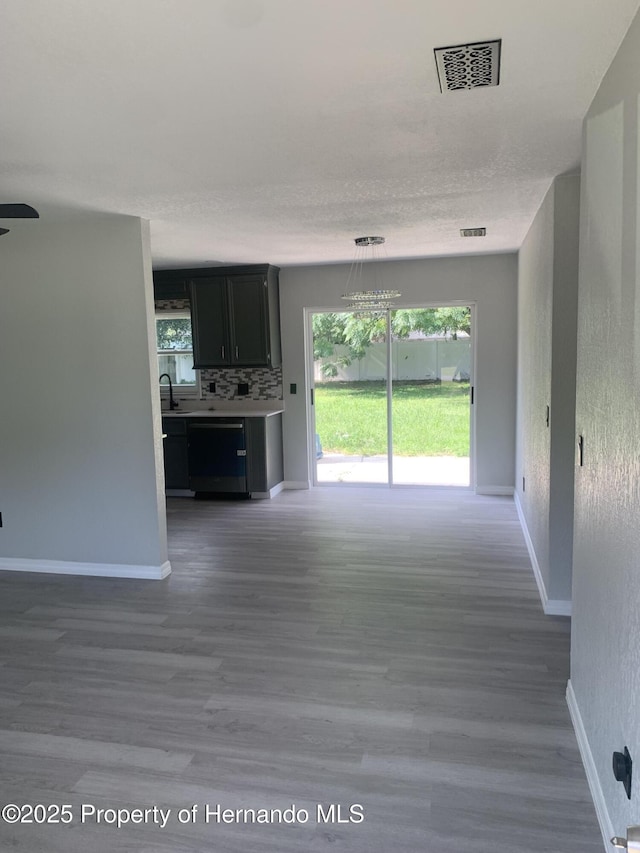 unfurnished living room featuring wood-type flooring, sink, a wealth of natural light, and an inviting chandelier