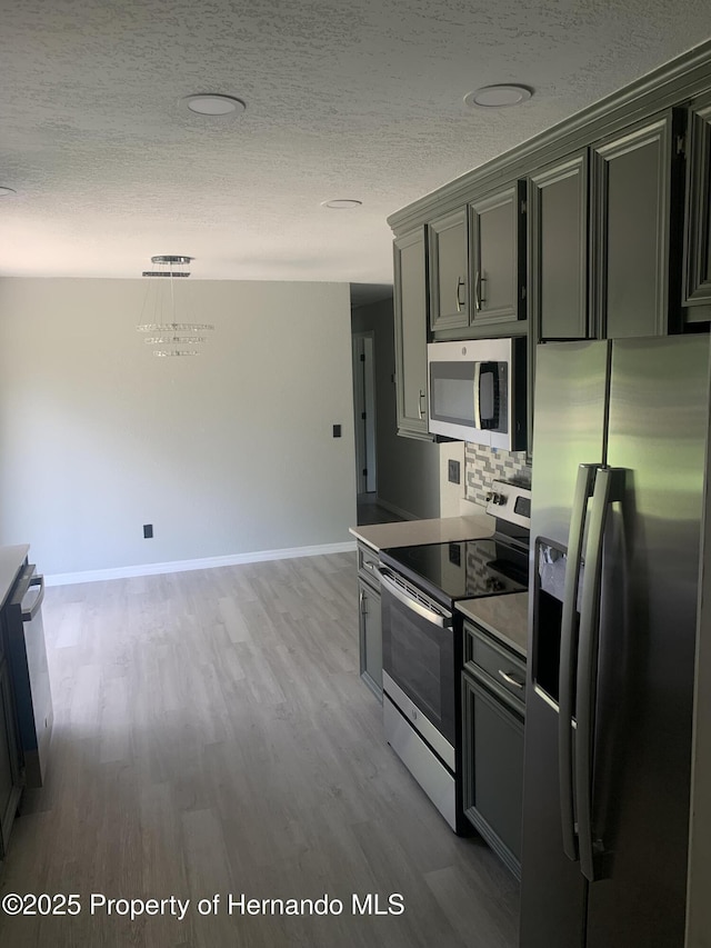 kitchen featuring appliances with stainless steel finishes, gray cabinetry, a textured ceiling, decorative light fixtures, and light hardwood / wood-style flooring