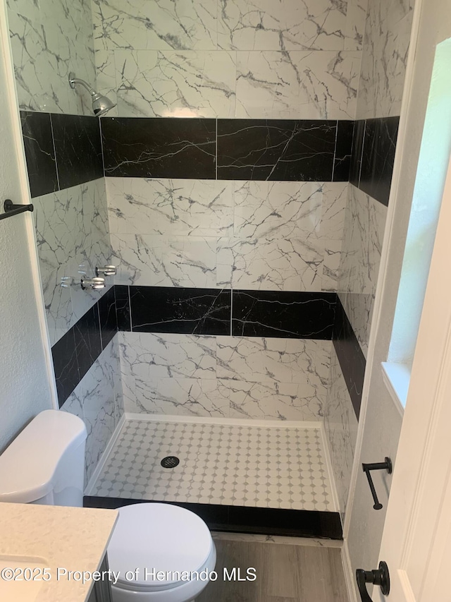 bathroom featuring toilet, a tile shower, and vanity