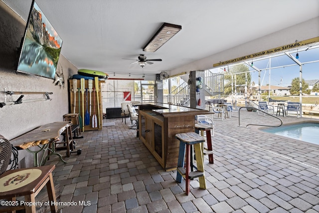 view of patio / terrace with ceiling fan, glass enclosure, and a bar